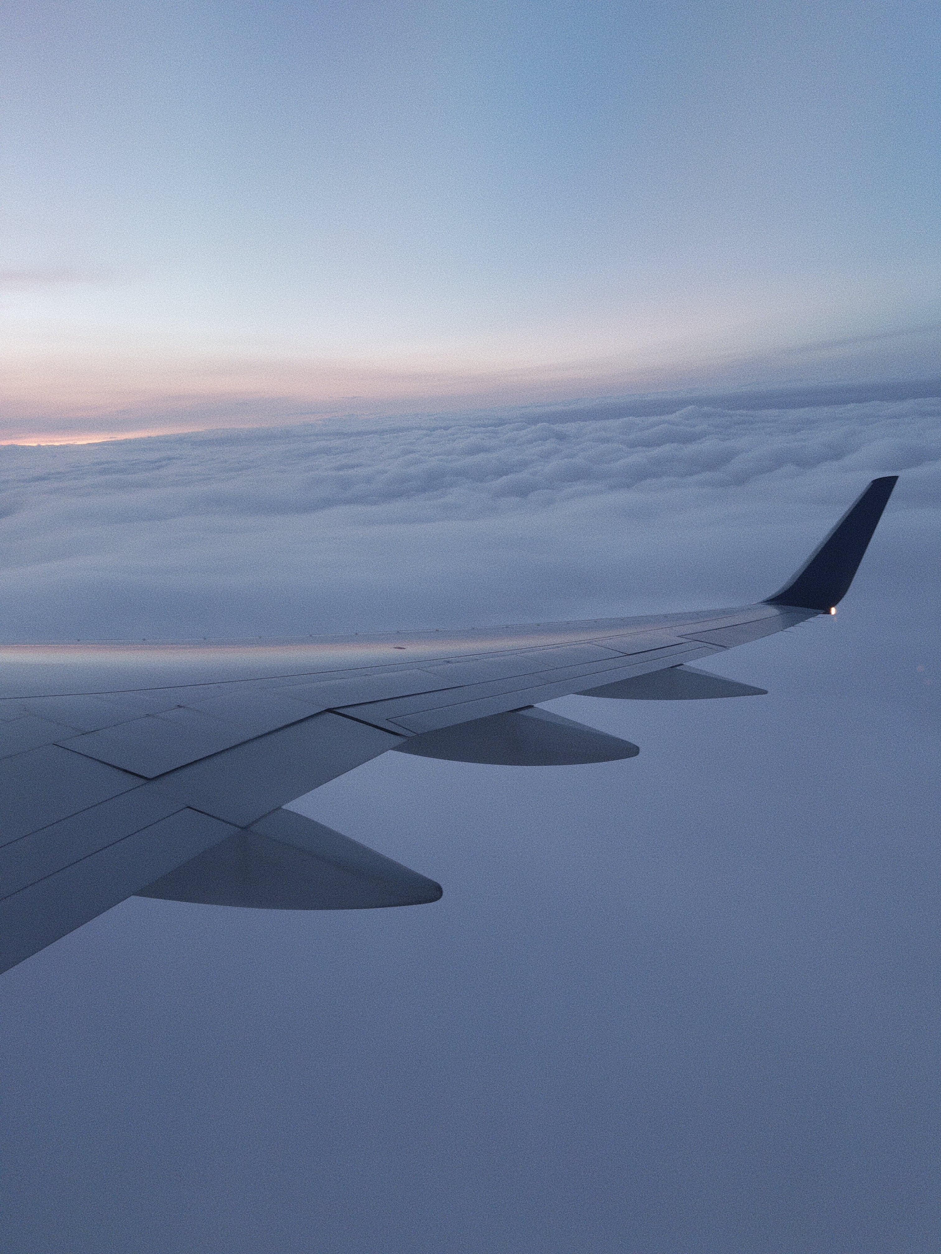 Picture of a plane wing above the clouds overlooking a sunset.